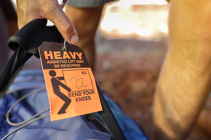 Know how to lift heavy objects without injury. person lifting large back with heavy warning tag